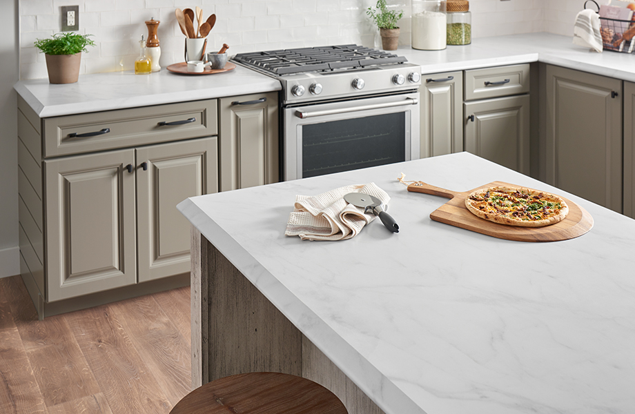 Kitchen with beige cabinets, a stove, kitchen utensils and an island with white marble Formica laminate countertops and pizza