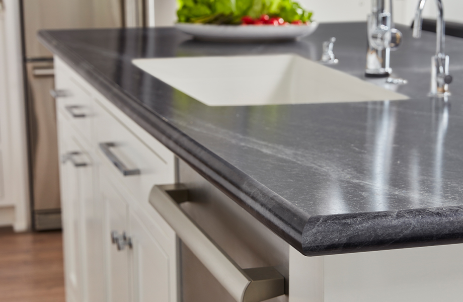 Corner of kitchen island with white cabinets, sink and black marbled Formica laminate countertop